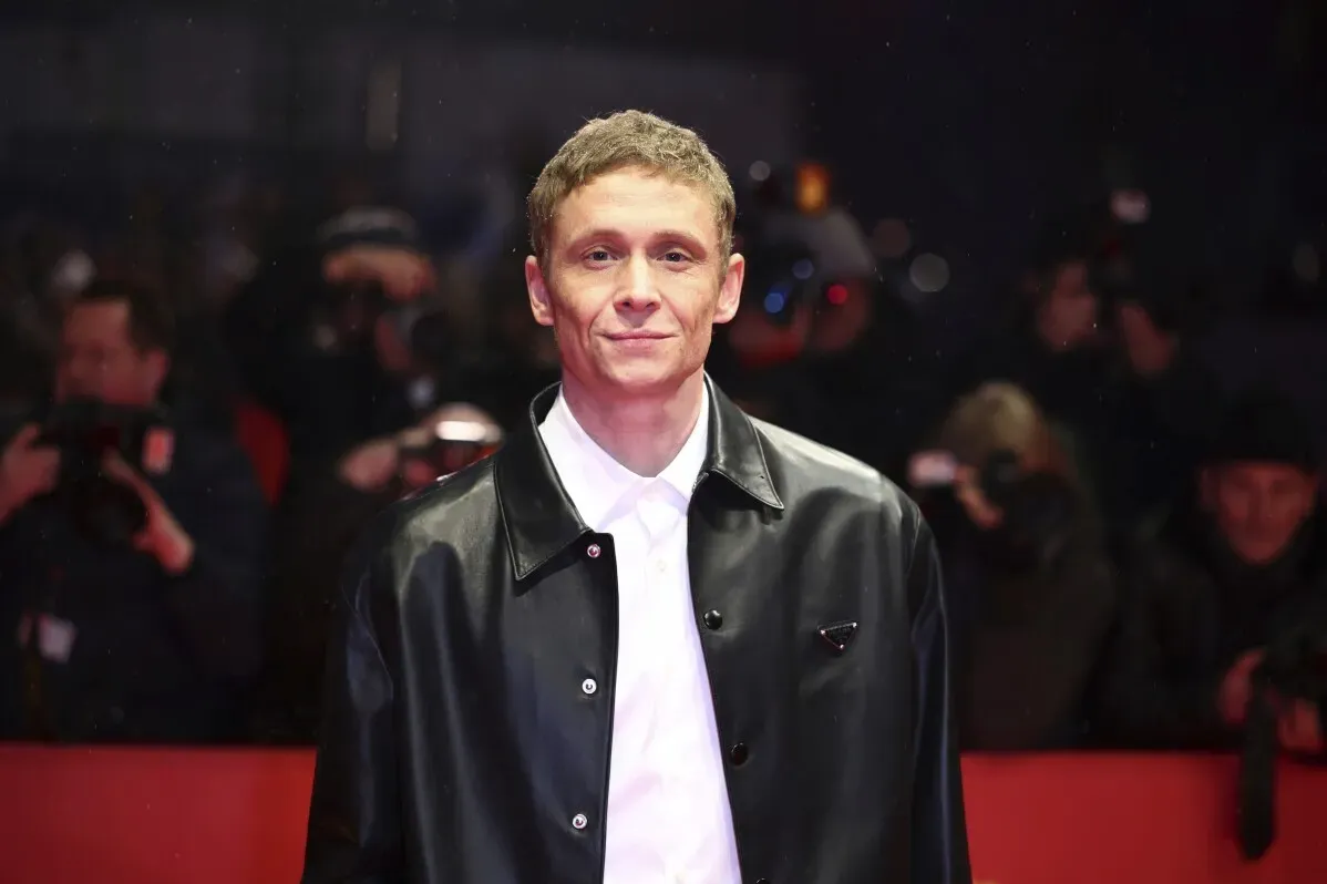مهرجان برلين السينمائي الدولي يفتتح بفيلم "الضوء" للمخرج توم تيكوير، حيث يظهر ممثل مبتسم يرتدي سترة جلدية، وسط حشد من المصورين.