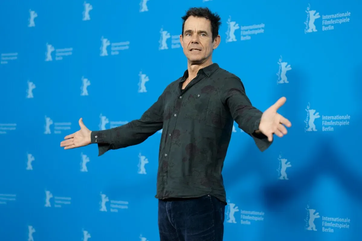 مخرج يقدم عرضًا في مهرجان برلين السينمائي الدولي، مع خلفية زرقاء تحمل شعار المهرجان، يعكس أجواء الفعالية السينمائية.