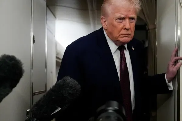 ترامب يظهر في ممر الطائرة، مع تعبير جاد، محاطًا بميكروفونات الصحفيين، بعد دعوى قضائية ضد بي بي سي تتعلق بتغطية خطابه.