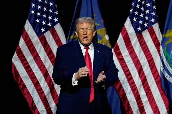 دونالد ترامب يتحدث في تجمع انتخابي، مع وجود علمين أمريكيين خلفه، معبرًا عن آراءه حول الرعاية الصحية والتغطية التأمينية.