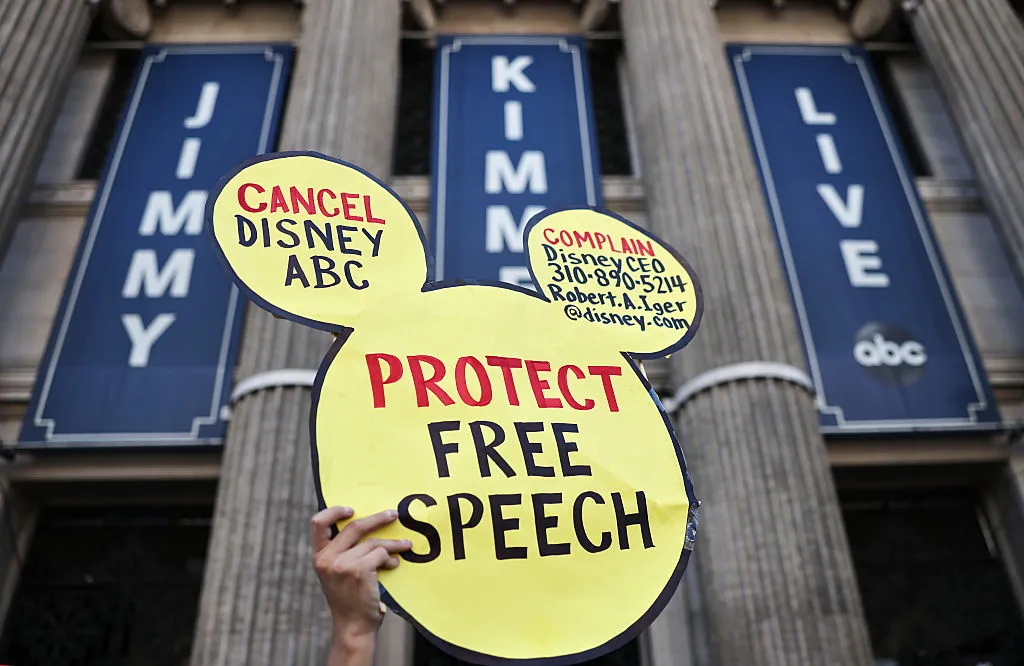 شخص يحمل لافتة على شكل أذني ميكي مكتوب عليها "حماية حرية التعبير" أمام مبنى برنامج Jimmy Kimmel Live على قناة ABC، تعبيراً عن احتجاجات ضد ديزني وتركيز ملكيتها الإعلامية.