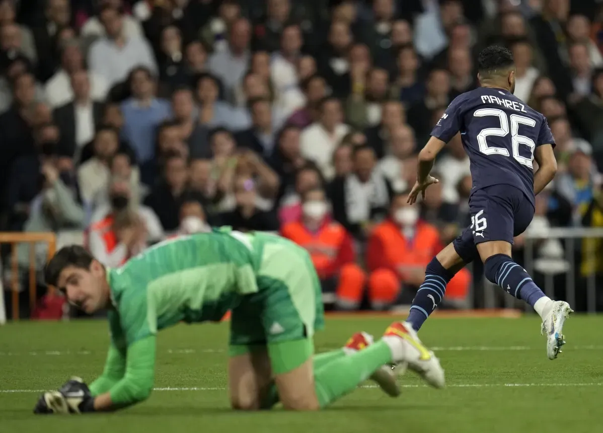 لاعب مانشستر سيتي رياض محرز يركض نحو المرمى بعد تمريرة، بينما حارس ريال مدريد تيبو كورتوا يحاول الانتصاب، في أجواء مشوقة لمباراة دوري أبطال أوروبا.