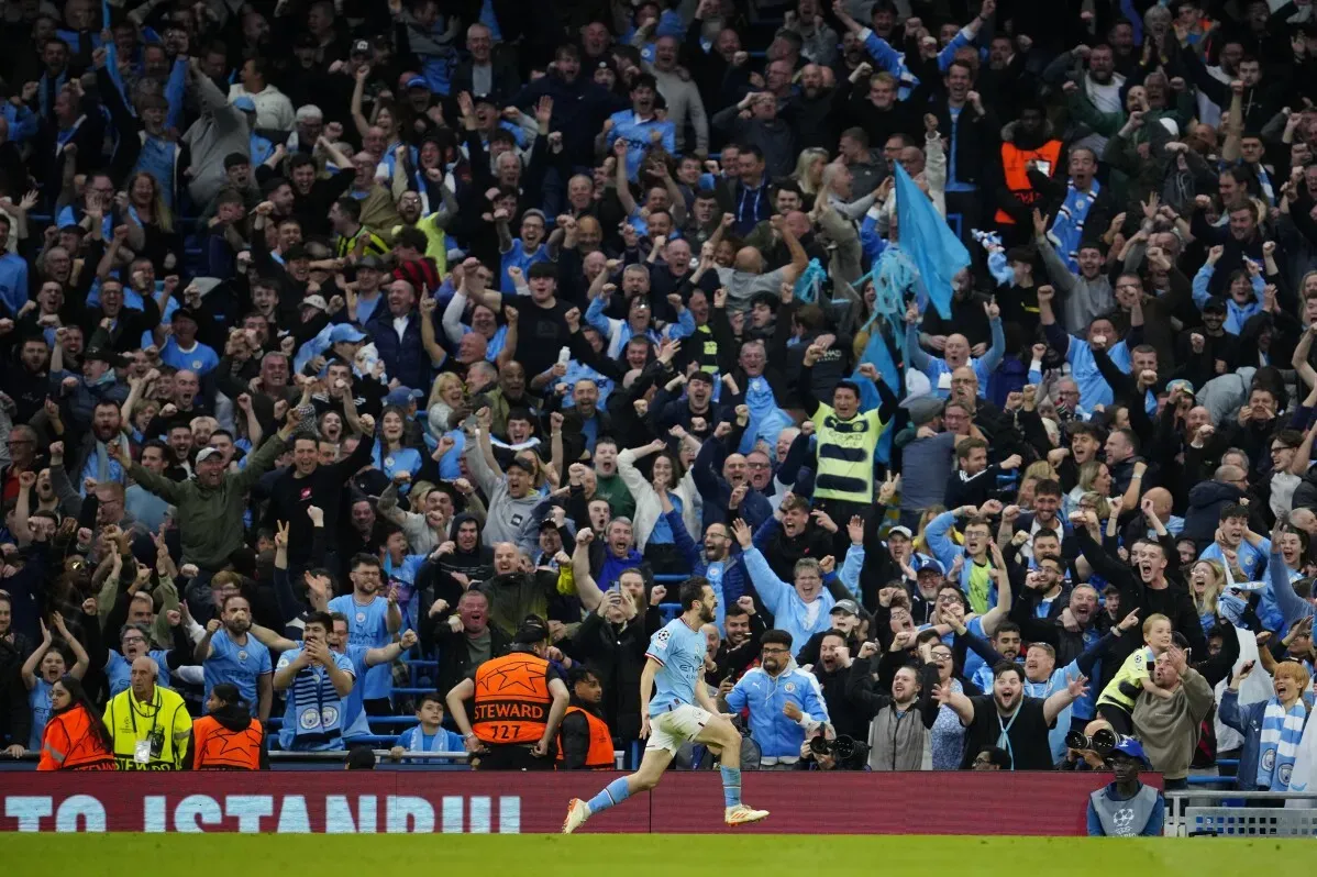 مشجعو مانشستر سيتي يحتفلون بحماس خلال مباراة دوري أبطال أوروبا، بينما يركض أحد اللاعبين نحوهم.