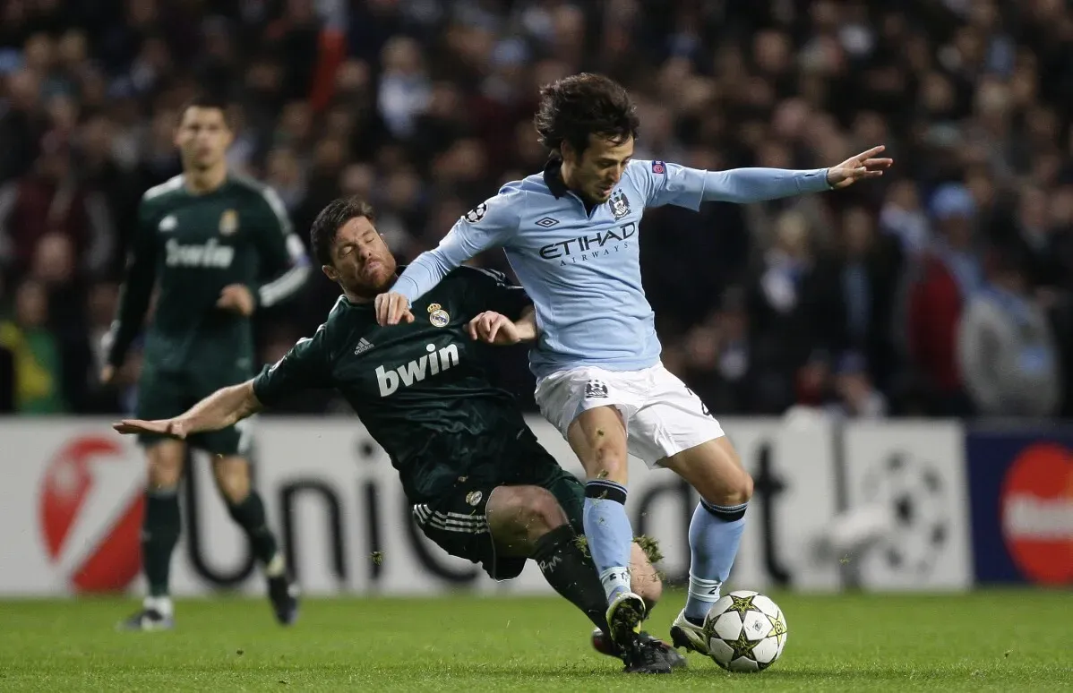 اللاعبان يتنافسان خلال مباراة كرة قدم بين ريال مدريد ومانشستر سيتي في دوري أبطال أوروبا، مع لمسات حاسمة ورهانات عالية.