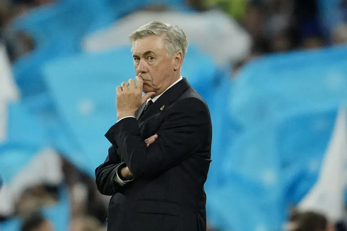 مدرب ريال مدريد كارلو أنشيلوتي، يبدو متأملاً أثناء المباراة، مع خلفية تظهر الجماهير. هذا اللقاء يمثل مواجهة هامة في دوري أبطال أوروبا.