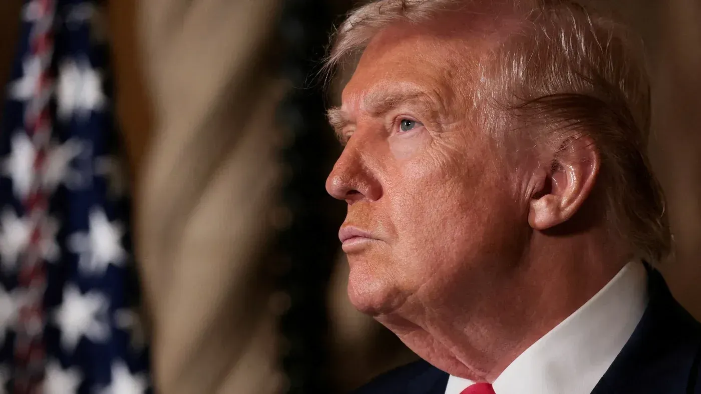 صورة لدونالد ترامب وهو ينظر إلى الجهة اليمنى، مع العلم الأمريكي في الخلفية، تعكس سياسته الجديدة حول "مجلس السلام".