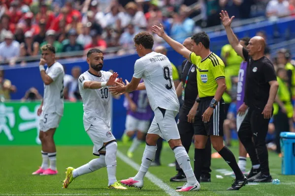 حمزة عبد الكريم، لاعب مصري شاب، يتبادل التحية مع زميله بعد دخوله الملعب في مباراة كأس العالم، مع أجواء حماسية من الجماهير.