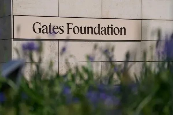 مؤسسة Gates تظهر في الصورة، مع التركيز على اسمها المكتوب بوضوح، محاطة بأزهار خضراء، مما يعكس جهودها في الصحة العالمية والتنمية.