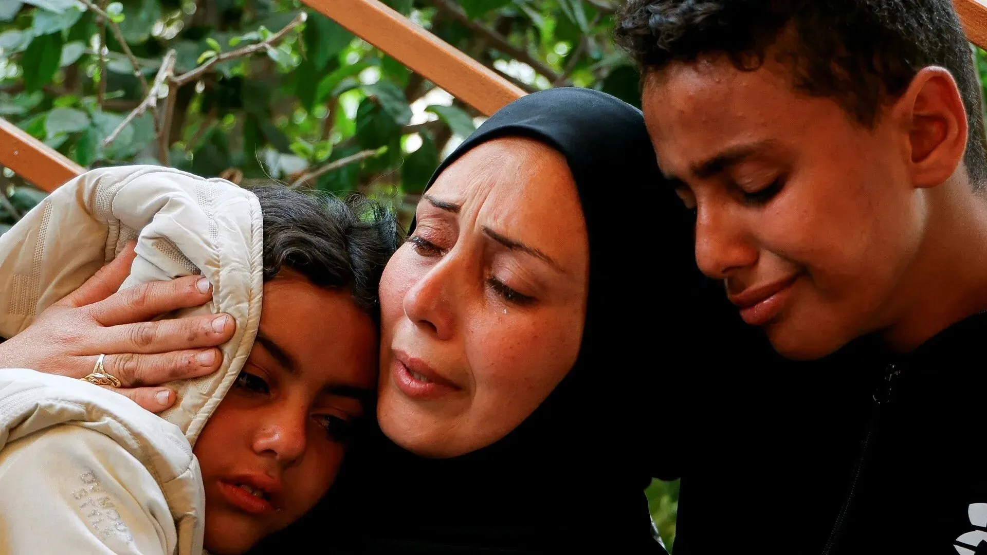 امرأة ترتدي الحجاب تحتضن طفلين، يعبرون عن مشاعر الحزن والقلق في سياق الصراع المستمر في غزة.
