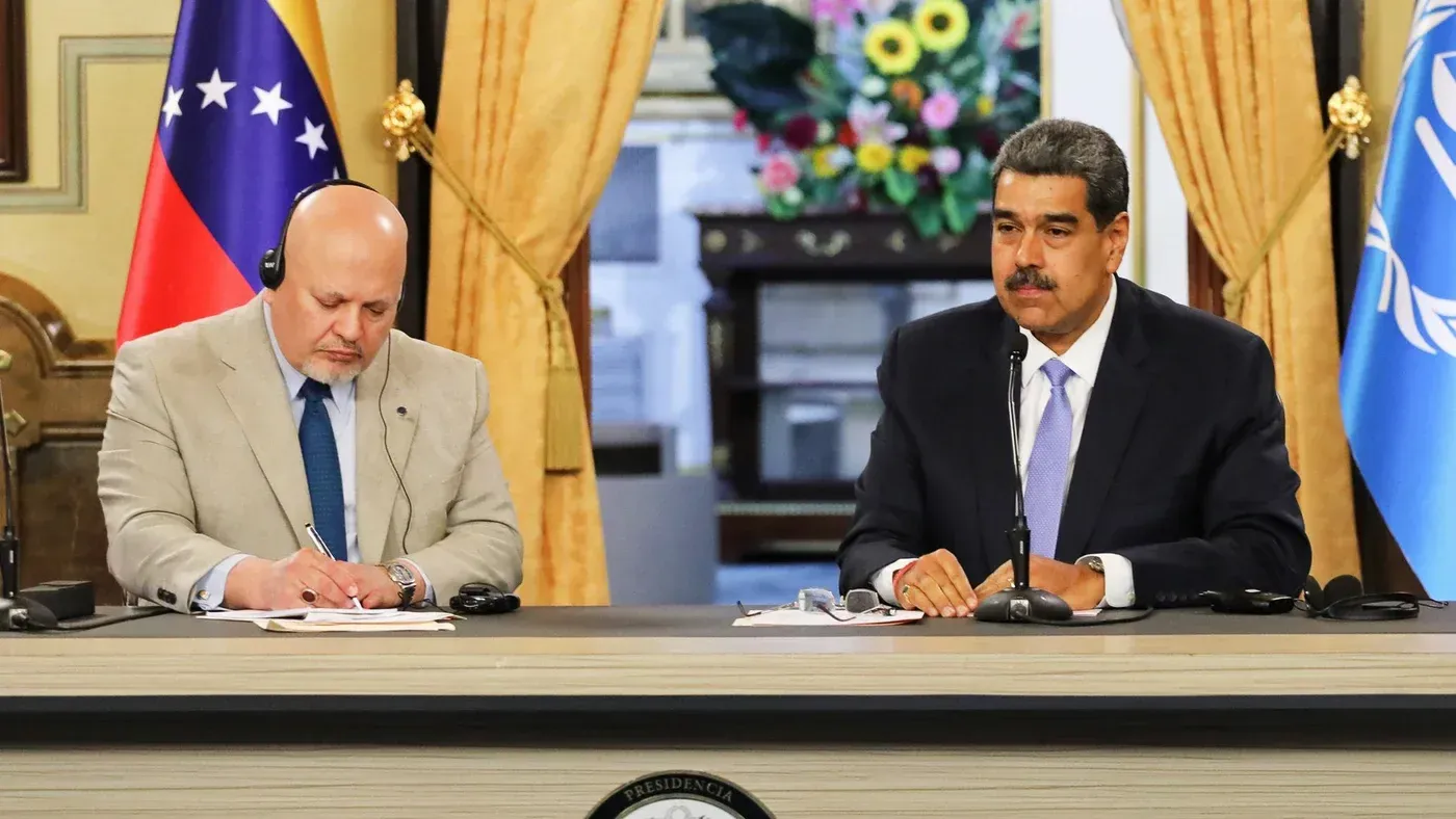 اجتماع بين المدعي العام للمحكمة الجنائية الدولية كريم خان والرئيس الفنزويلي نيكولاس مادورو، مع العلم الفنزويلي وشعار الأمم المتحدة في الخلفية.