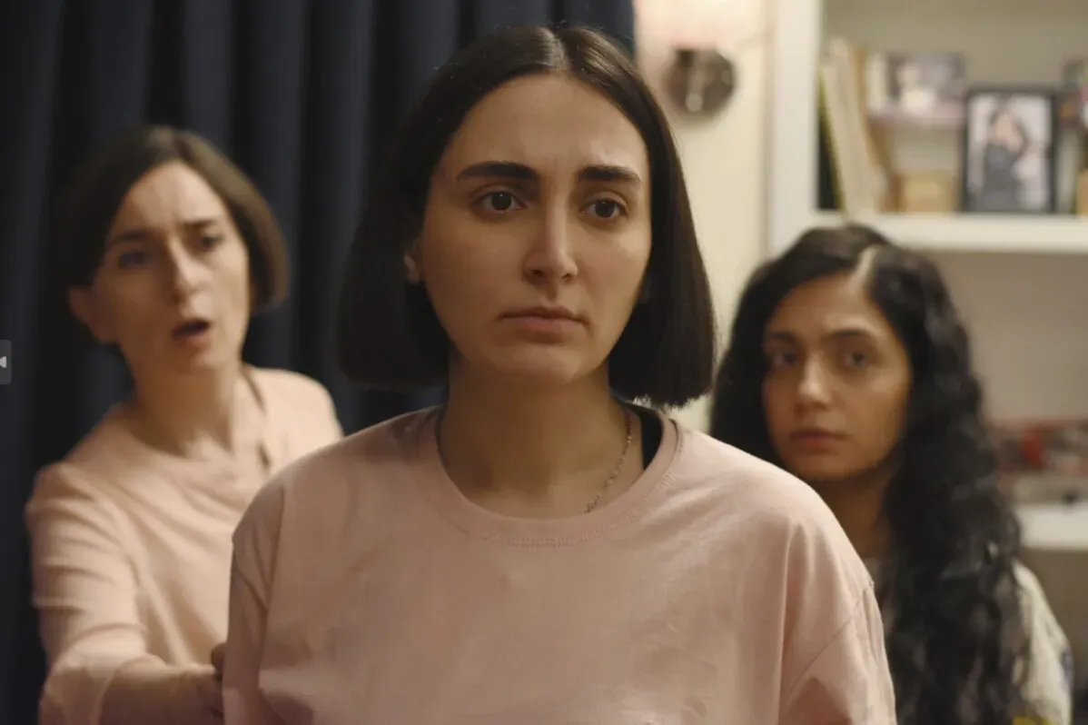 ثلاث نساء في مشهد درامي، حيث تبدو واحدة منهن بقلق واضح، بينما الأخريتان تعبران عن مشاعر مختلفة، مما يعكس التوتر في العلاقات الإنسانية.