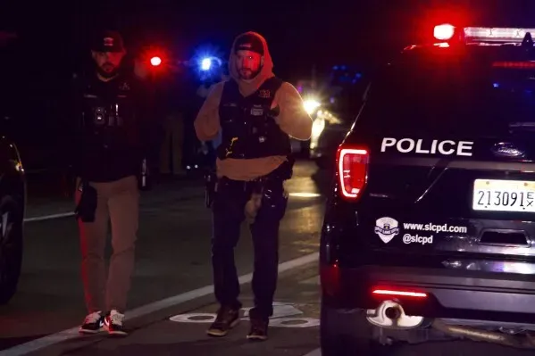 رجال شرطة يرتدون سترات واقية يتفقدون موقع حادث إطلاق نار بالقرب من كنيسة في مدينة سولت ليك سيتي، مع وجود أضواء الطوارئ في الخلفية.