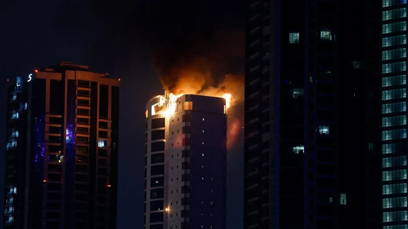 اندلاع حريق في أحد المباني المرتفعة في البحرين، مع تصاعد الدخان والنيران، وسط أضواء المباني المجاورة.