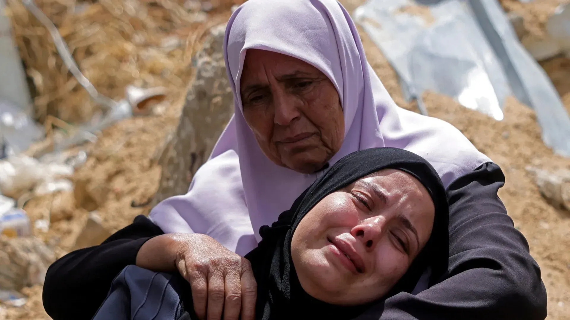 امرأتان فلسطينيتان تحتضنان بعضهما البعض في لحظة حزن عميق، تعكسان الألم والمعاناة الناتجة عن الصراع المستمر في غزة.