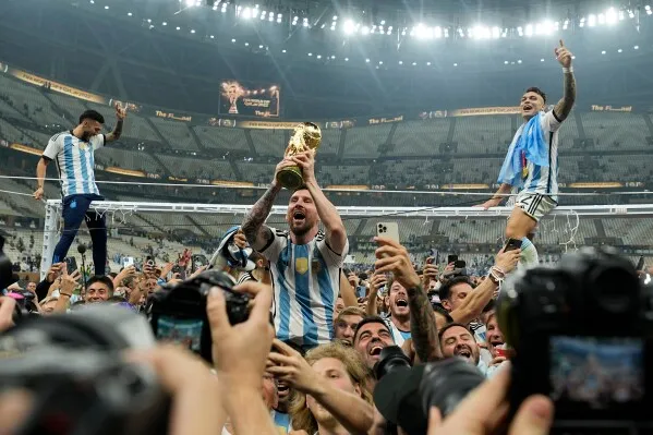 فرحة لاعبي الأرجنتين بعد الفوز بكأس العالم، حيث يحمل أحدهم الكأس وسط احتفالات جماهيرية حماسية في الملعب.