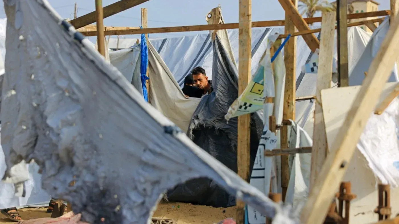 رجل يقف داخل مخيم مؤقت في المواصي بجنوب غزة، محاط بخيام ممزقة، مما يعكس معاناة الأسر النازحة في ظل استمرار النزاع.