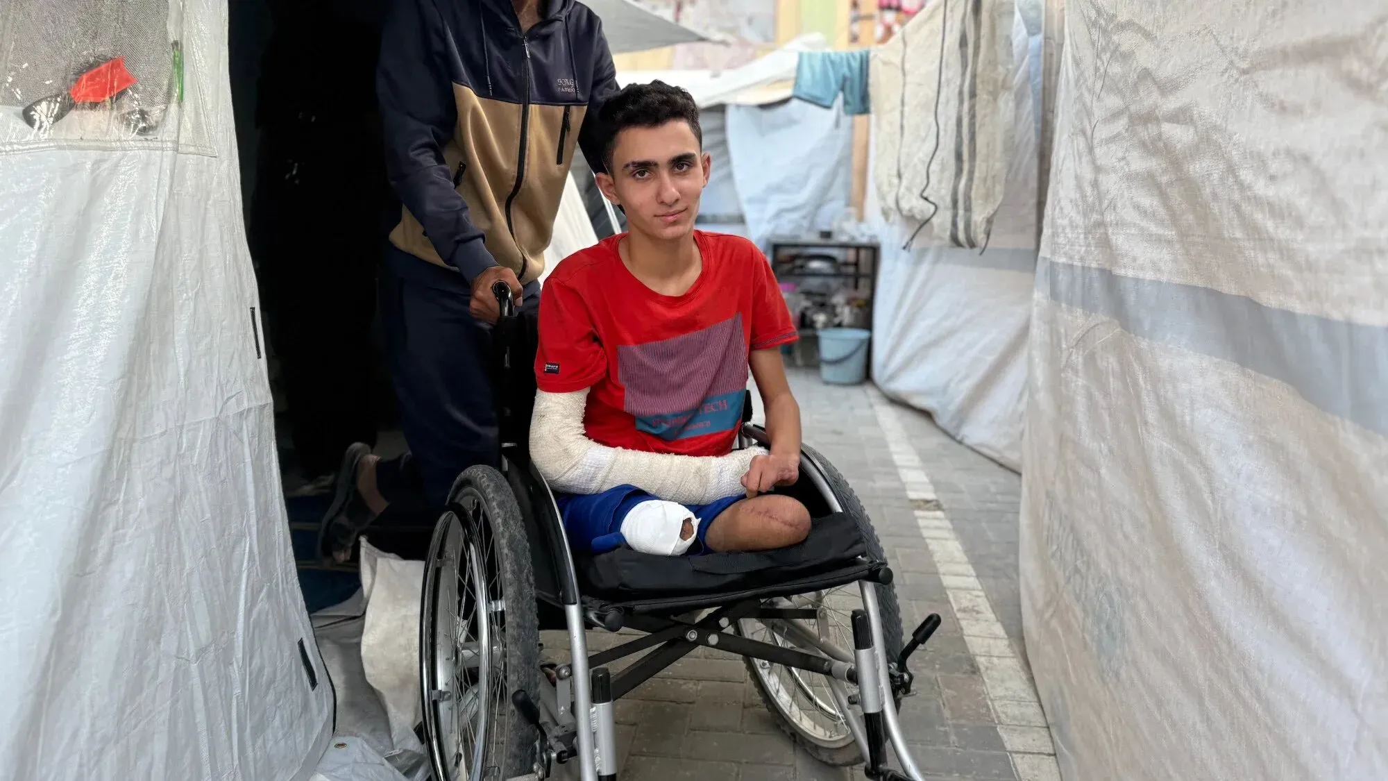 أحمد الغلبان، شاب فلسطيني، يجلس على كرسي متحرك في مخيم للاجئين، بعد بتر ساقيه نتيجة القصف، في ظل ظروف الحرب في غزة.