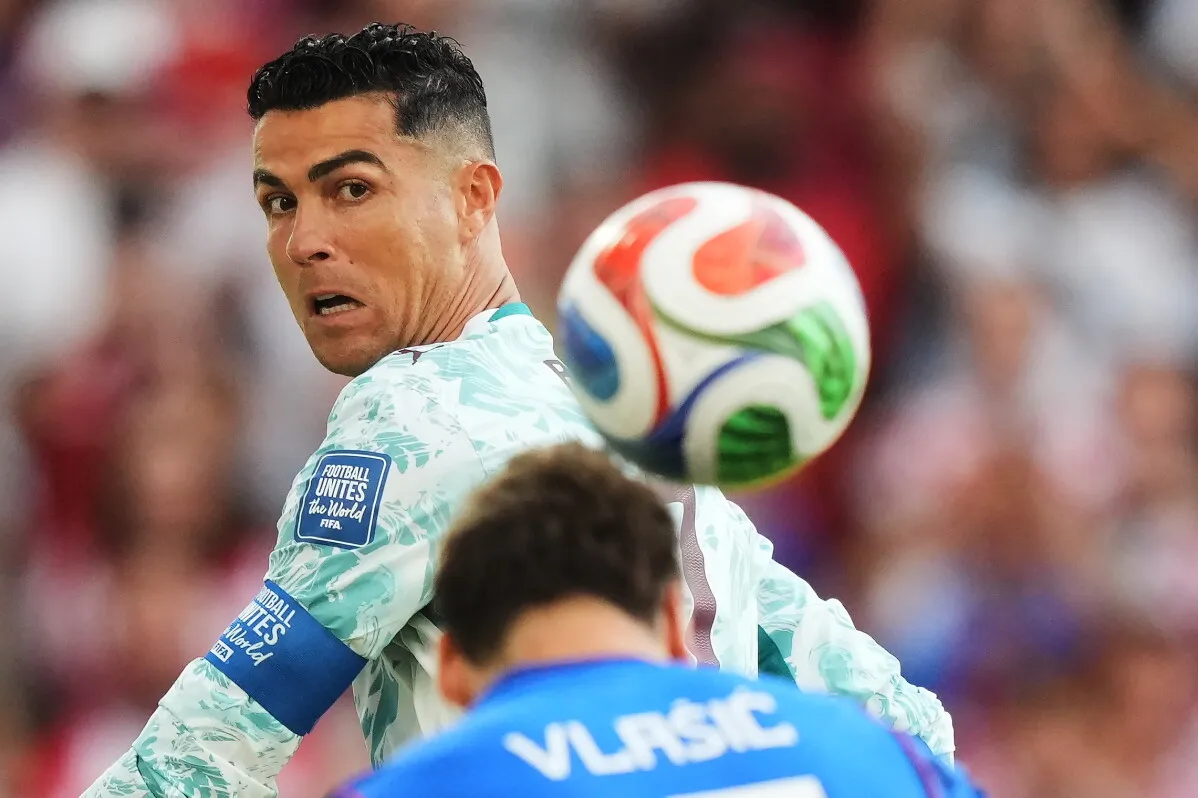 لاعب كرة قدم يرتدي شارة القيادة يراقب كرة متصلة ملونة أثناء مباراة كأس العالم، مع ظهور لاعب منافس في الخلفية.