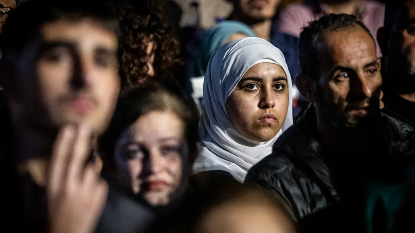 شابة فلسطينية ترتدي الحجاب وسط مجموعة من الأشخاص، تعبير وجهها يعكس القلق والتوتر في سياق التمييز العنصري ضد الفلسطينيين في أماكن العمل بإسرائيل.