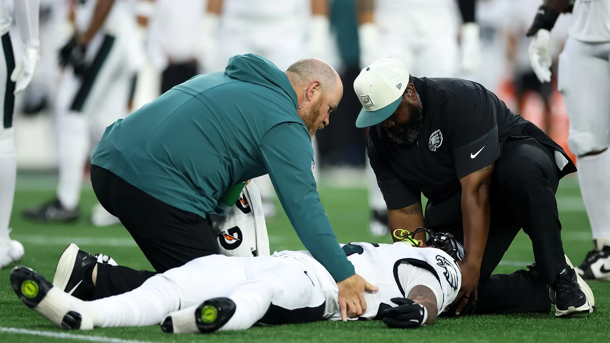 لاعب كرة قدم أمريكي ملقى على الأرض يتلقى الإسعافات الأولية من مدربين أثناء مباراة NFL، مع التركيز على مخاطر إصابات الدماغ المرتبطة بالرياضة.