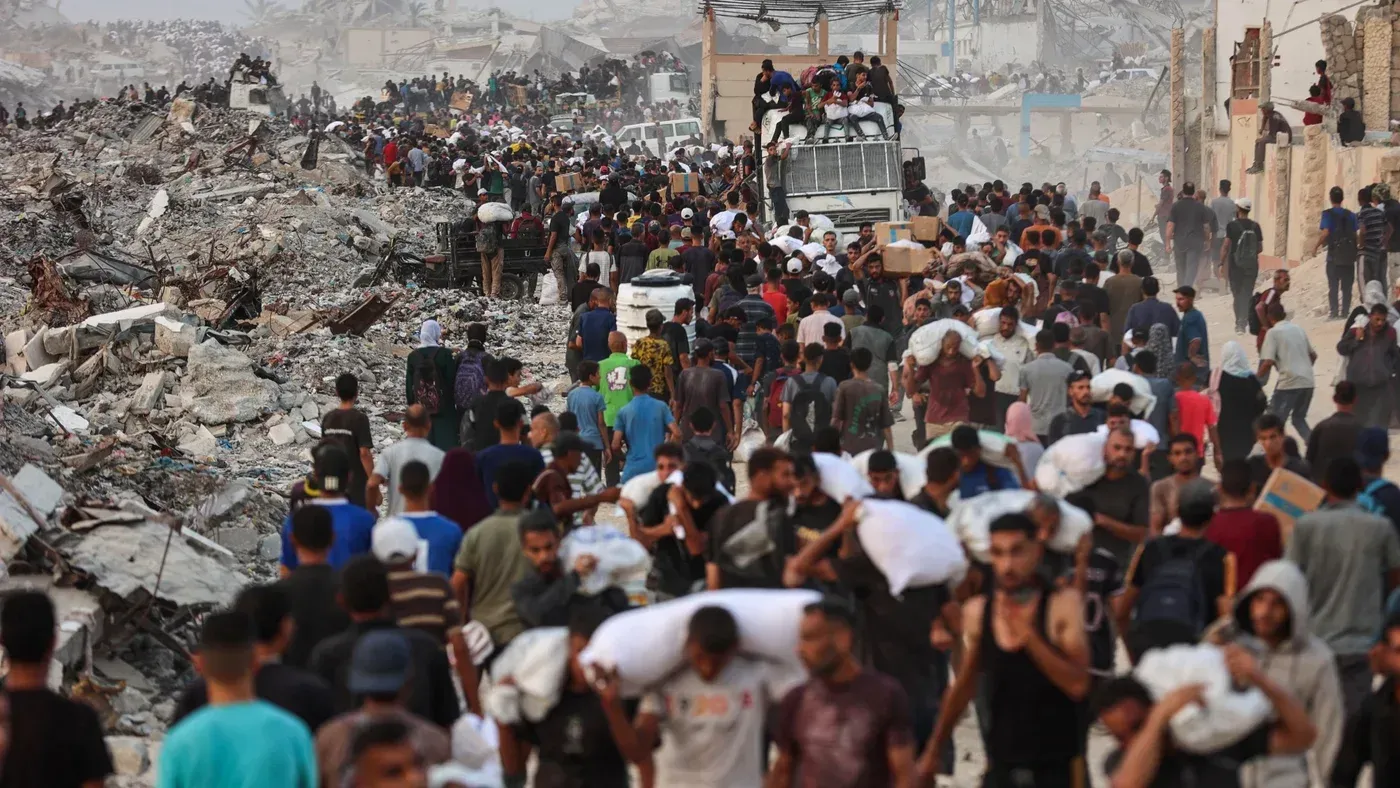 تجمع حشود من الفلسطينيين في منطقة مدمرة في رفح، حيث يحمل الكثيرون الإمدادات. تعكس الصورة الأوضاع الإنسانية المأساوية في غزة.
