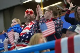 مشجعون أمريكيون يرتدون ملابس تحمل الألوان الوطنية، يحملون أعلامًا صغيرة، يعبرون عن حماسهم خلال منافسات الكيرلنج في أولمبياد كورتينا.