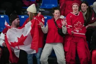 مشجعو فريق الكيرلنج الكندي يحتفلون بفوزهم بالميدالية البرونزية في أولمبياد كورتينا، مرتدين ملابس حمراء وحاملة علم كندا.