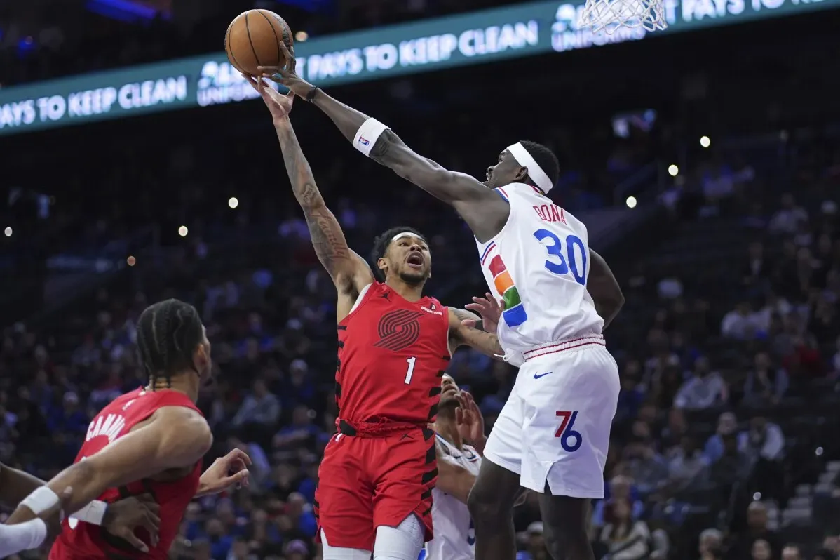 لاعب بورتلاند تريل بليزرز يسجل نقطة مع محاولة دفاعية من لاعب فيلادلفيا 76ers في مباراة كرة السلة، حيث تميز سيمونز بأداء قوي.