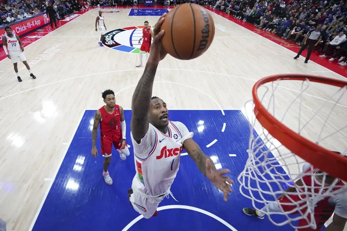 لاعب من فريق 76ers يسجل سلة أثناء مباراة ضد بورتلاند تريل بليزرز، مع وجود لاعبين آخرين في الخلفية.