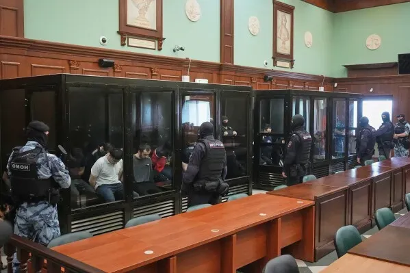 محاكمة 19 متهمًا بالتورط في هجوم موسكو، مع وجود أفراد الأمن حولهم في قاعة المحكمة، حيث تظهر الأجواء المشددة.