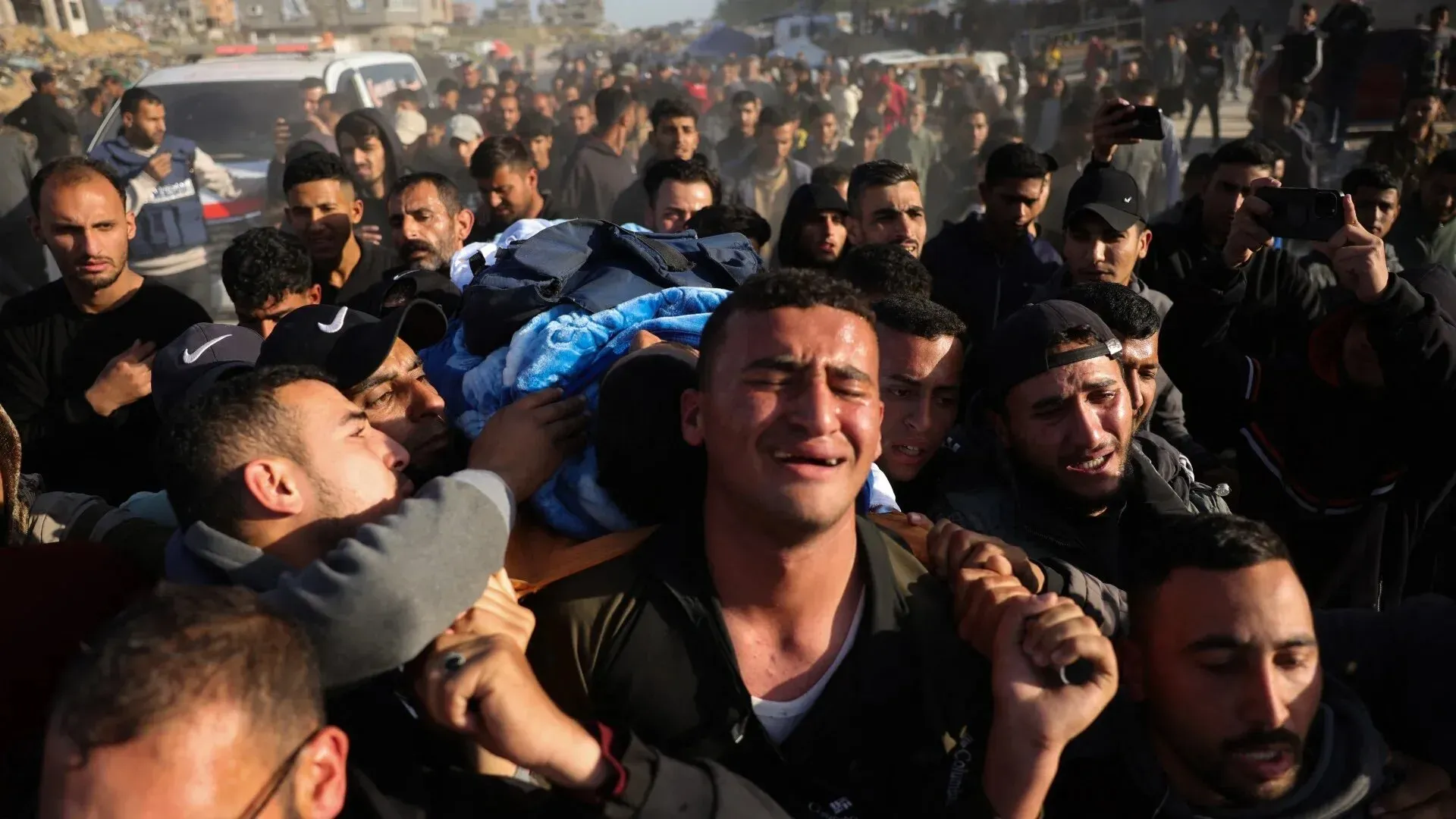 مشيعون فلسطينيون يحملون جثمان محمد منصور وسط حشود من المعزين، مع تعبيرات حزن واضحة على وجوههم في مشهد يعكس مأساة فقدان الصحفيين.