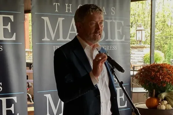 توماس ماسي يتحدث في فعالية انتخابية، مع لافتة خلفه تدعمه كمرشح للكونغرس، بينما يركز على أجندة الرئيس ترامب.