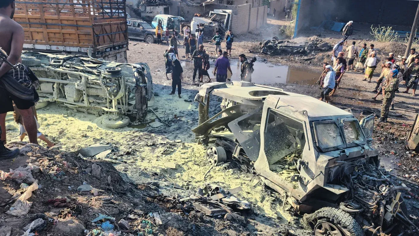 صورة تظهر موقع انفجار في اليمن، مع سيارات مدمرة وأشخاص يتجمعون في الخلفية، مما يعكس الأثر المدمر للصراع المستمر.