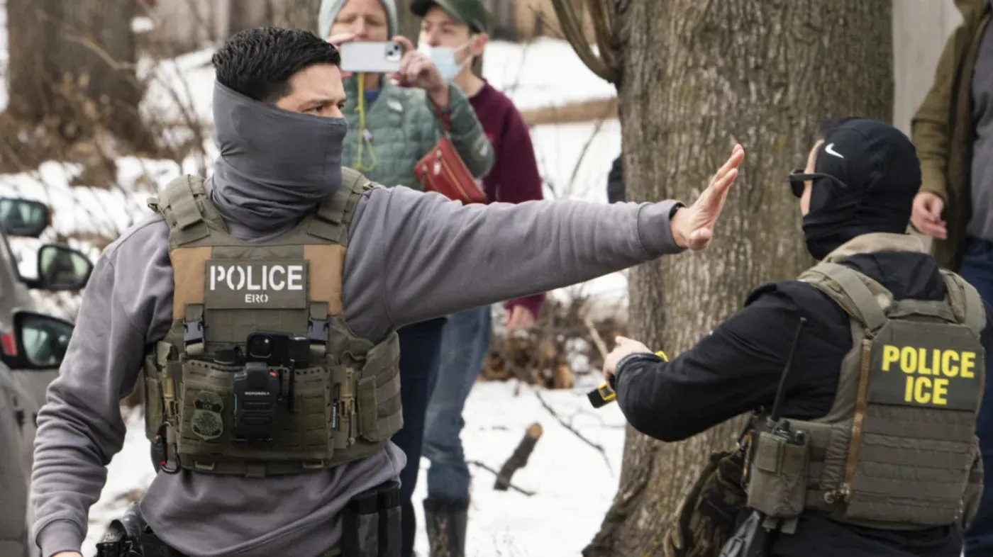 صورة لرجال شرطة يرتدون زيًا رسميًا أثناء تنفيذ عملية اعتقال للاجئين في مينيسوتا، وسط أجواء شتوية.