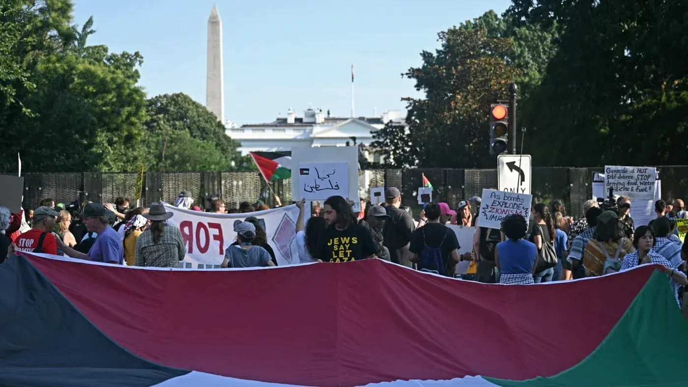 تجمع حشود من المتظاهرين في واشنطن حاملين لافتات تعبر عن دعمهم لفلسطين، مع العلم الفلسطيني الكبير في المقدمة.