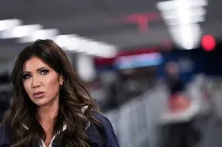 السكرتيرة الصحفية للبيت الأبيض كارولين ليفيت تتحدث بجدية في مؤتمر صحفي، مع خلفية مضاءة بأضواء صناعية.