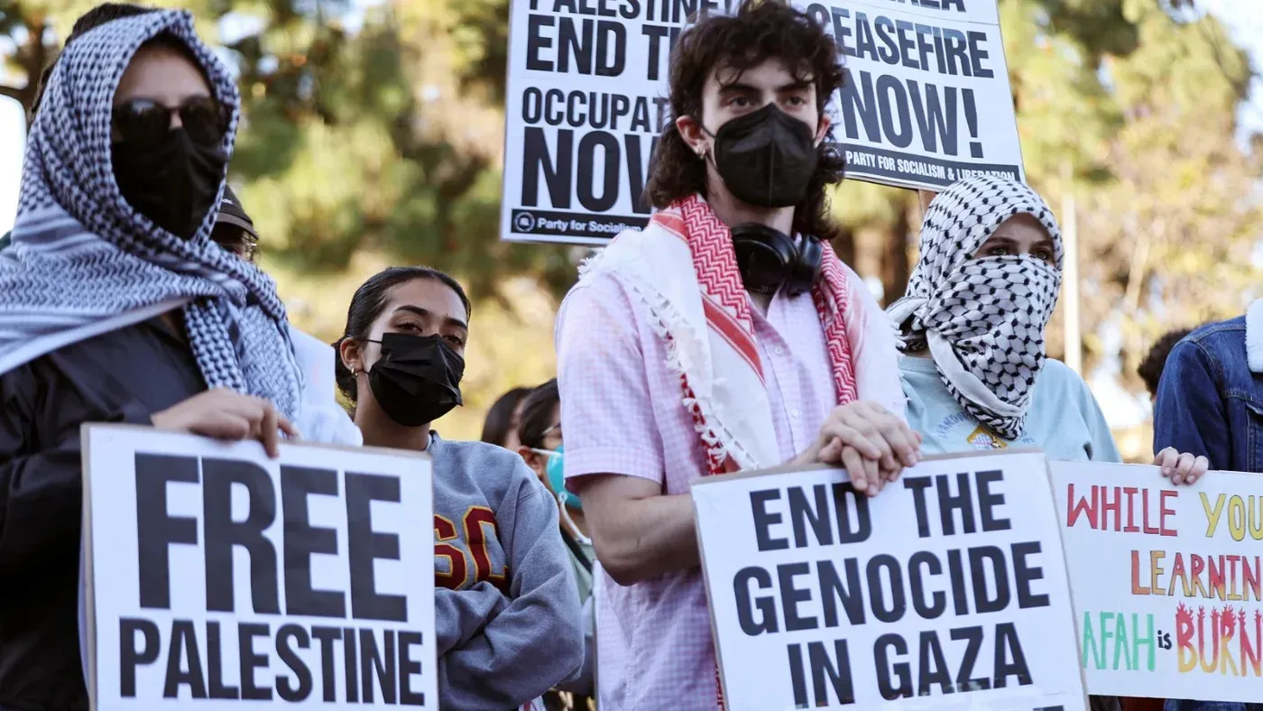 محتجون مرتدون كمامات ومنديل فلسطيني يحملون لافتات تدعو إلى إنهاء الاحتلال ودعم فلسطين في أحد المظاهرات الجامعية.