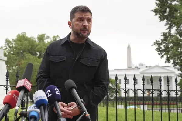 الرئيس الأوكراني فولوديمير زيلينسكي يتحدث للصحفيين أمام البيت الأبيض، مع وجود أعلام وكاميرات في الخلفية، وسط أجواء سياسية متوترة.