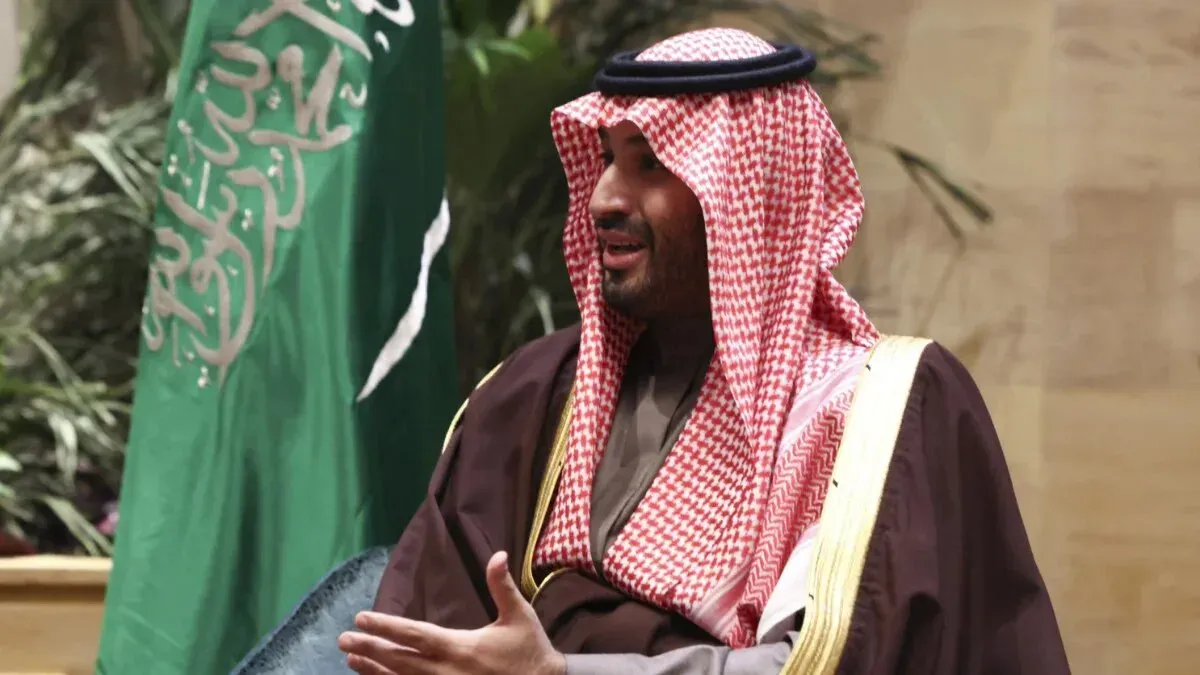 الأمير محمد بن سلمان يتحدث أثناء اجتماع، مع العلم السعودي في الخلفية، في إطار مناقشات حول العلاقات السعودية الأمريكية وصفقات الأسلحة.