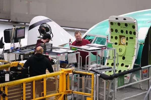 عمال في مصنع Boeing يقومون بأعمال تجميع لطائرة، مع التركيز على تفاصيل الإنتاج والتقنيات المستخدمة في عملية التصنيع.