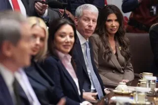 اجتماع رسمي يظهر مجموعة من المسؤولين، مع التركيز على امرأة ترتدي بدلة، تعكس الأجواء السياسية الجادة في الولايات المتحدة.