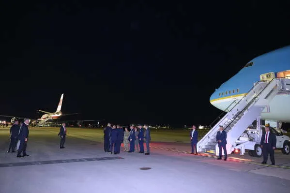 مجموعة من المسؤولين الأمنيين والسياسيين يقفون بجانب طائرة Air Force One الرئاسية في مطار ليلاً خلال رحلة سرية للرئيس ترامب وسط تهديدات أمنية.
