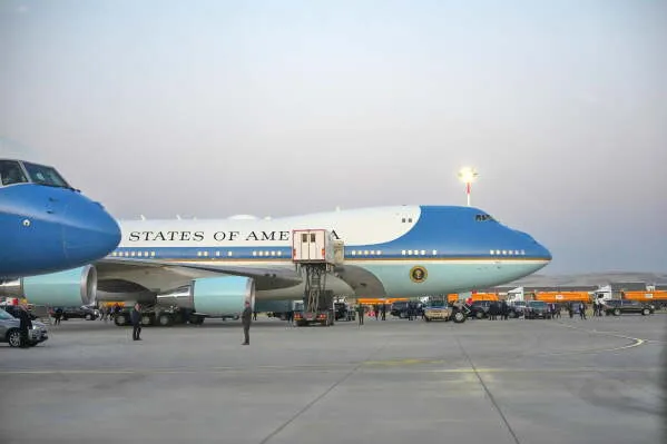 طائرة Air Force One الزرقاء القديمة متوقفة على مدرج في مطار أثناء غروب الشمس، مع وجود أفراد أمن ومعدات دعم حولها في سياق رحلة سرية للرئيس الأمريكي ترامب.