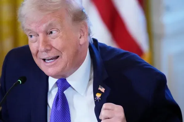 دونالد ترامب يظهر وهو يرفع طية صدر سترته ليعرض دبوسًا يحمل صورته الكاريكاتورية، بجانب دبوس العلم الأمريكي، خلال فعالية في البيت الأبيض.