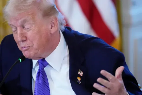 دونالد ترامب يتحدث خلال فعالية في البيت الأبيض، مرتديًا دبوسًا يحمل صورته الكاريكاتورية تحت دبوس العلم الأمريكي.