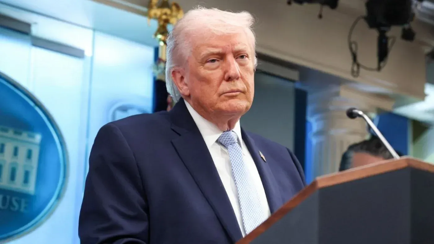 دونالد ترامب يتحدث في مؤتمر صحفي، مع التركيز على تعبير وجهه الجاد، وسط خلفية رسمية. يناقش قضايا استراتيجية تتعلق بإيران.