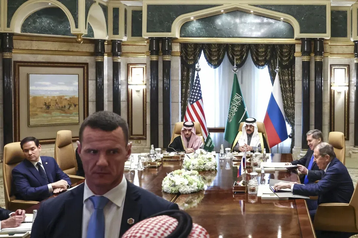 اجتماع دبلوماسي في السعودية بين ممثلين من الولايات المتحدة وروسيا، مع وجود أعلام البلدين، يناقش قضايا الحرب في أوكرانيا.