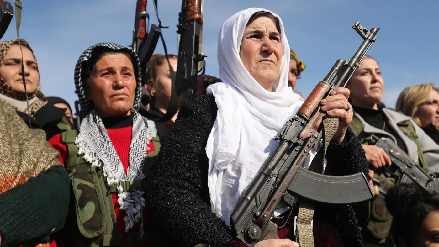 نساء من قوات سوريا الديمقراطية يحملن أسلحة ويظهرن في تجمع، تعبيرات وجوههن تعكس القوة والتصميم في مواجهة التحديات.