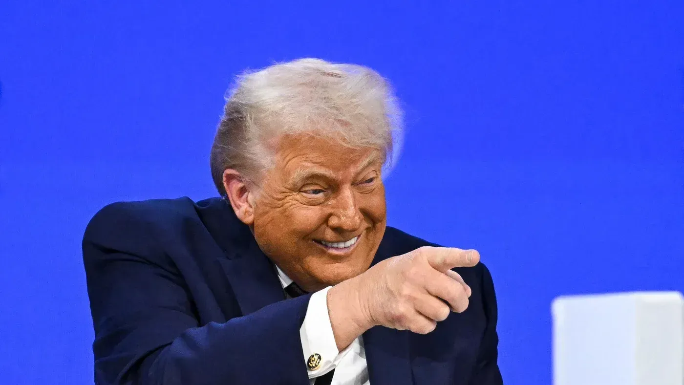 ترامب مبتسم أثناء حديثه في اجتماع "مجلس السلام" في واشنطن، مع خلفية زرقاء، حيث يناقش خطة وقف إطلاق النار لغزة.