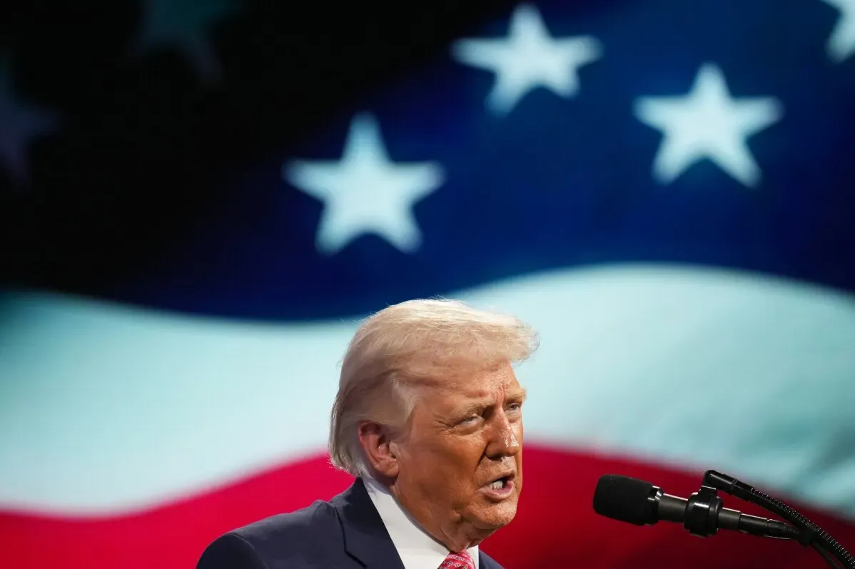 ترامب يتحدث أمام ميكروفون مع العلم الأمريكي خلفه، مشيرًا إلى التوترات مع إيران وتأثيرها على السياسة الأمريكية.